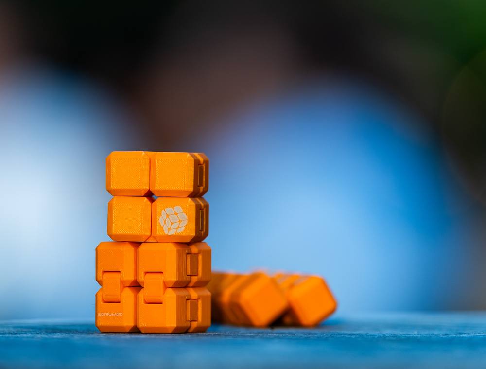 Orangener CUBY-Stapel vor grau-blauem Hintergrund, daneben liegende Würfel